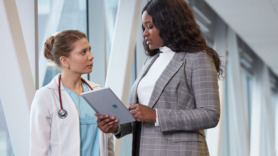 Two co-workers interact with a Surface Pro device in the hallway of a hospital