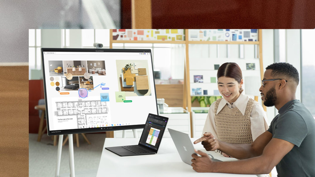 Dos compañeros de trabajo interactúan con dos dispositivos Surface Laptop 5 con un dispositivo Surface Hub 2S en el fondo