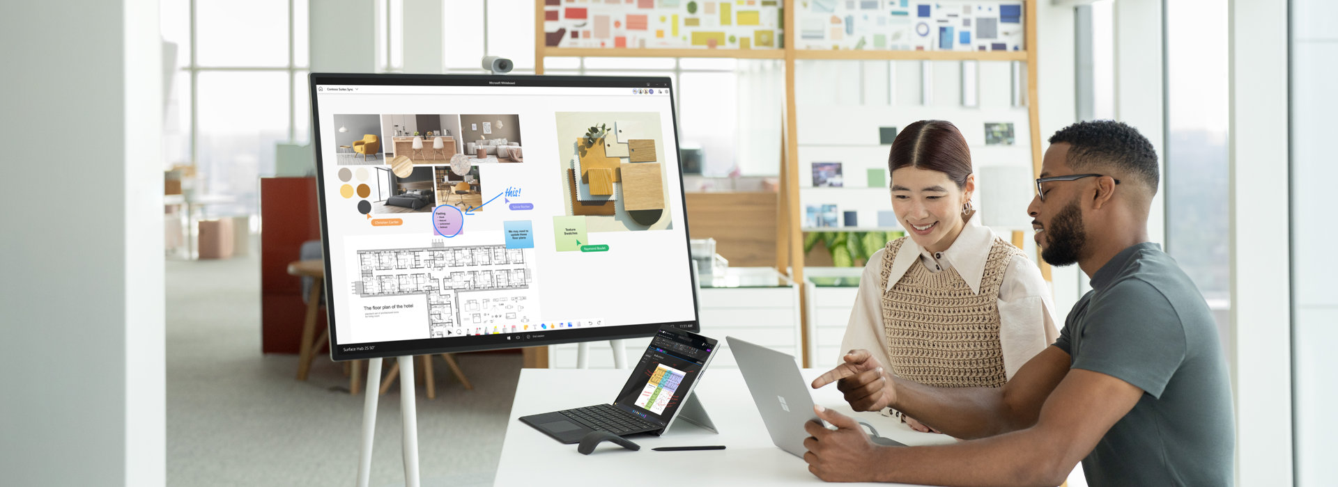 Surface Hub 2S が背景に置かれた状態で、2 台の Surface Laptop 5 デバイスでやり取りをする 2 人の同僚