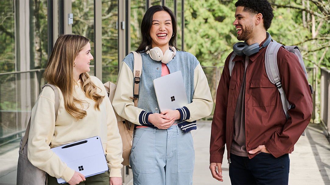 Two females and one male standing outside glass doors to a building and carrying a Surface Pro and a Surface Laptop