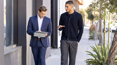 Two men walking down a sidewalk and using a Surface Pro and Surface Slim Pen