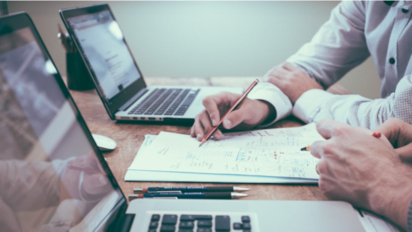 Two people completing homework while using their laptops and pen and paper