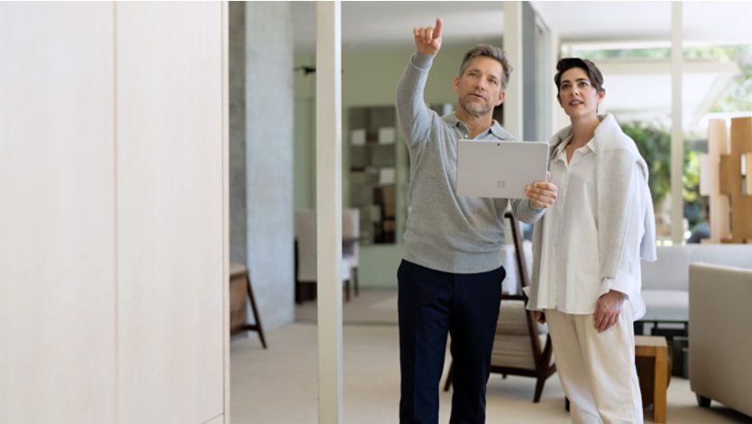 A man directs a woman to look by pointing his finger while holding a platinum Surface Pro 9