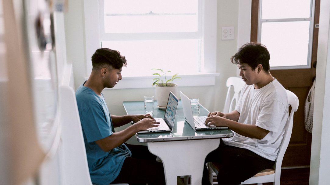 Two young men sitting at a table with their computers