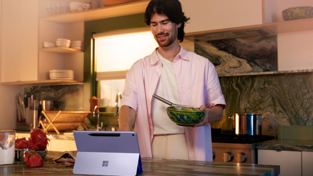 A man in the kitchen in the middle of cooking with a Surface Pro 2-in-1 laptop on the kitchen counter