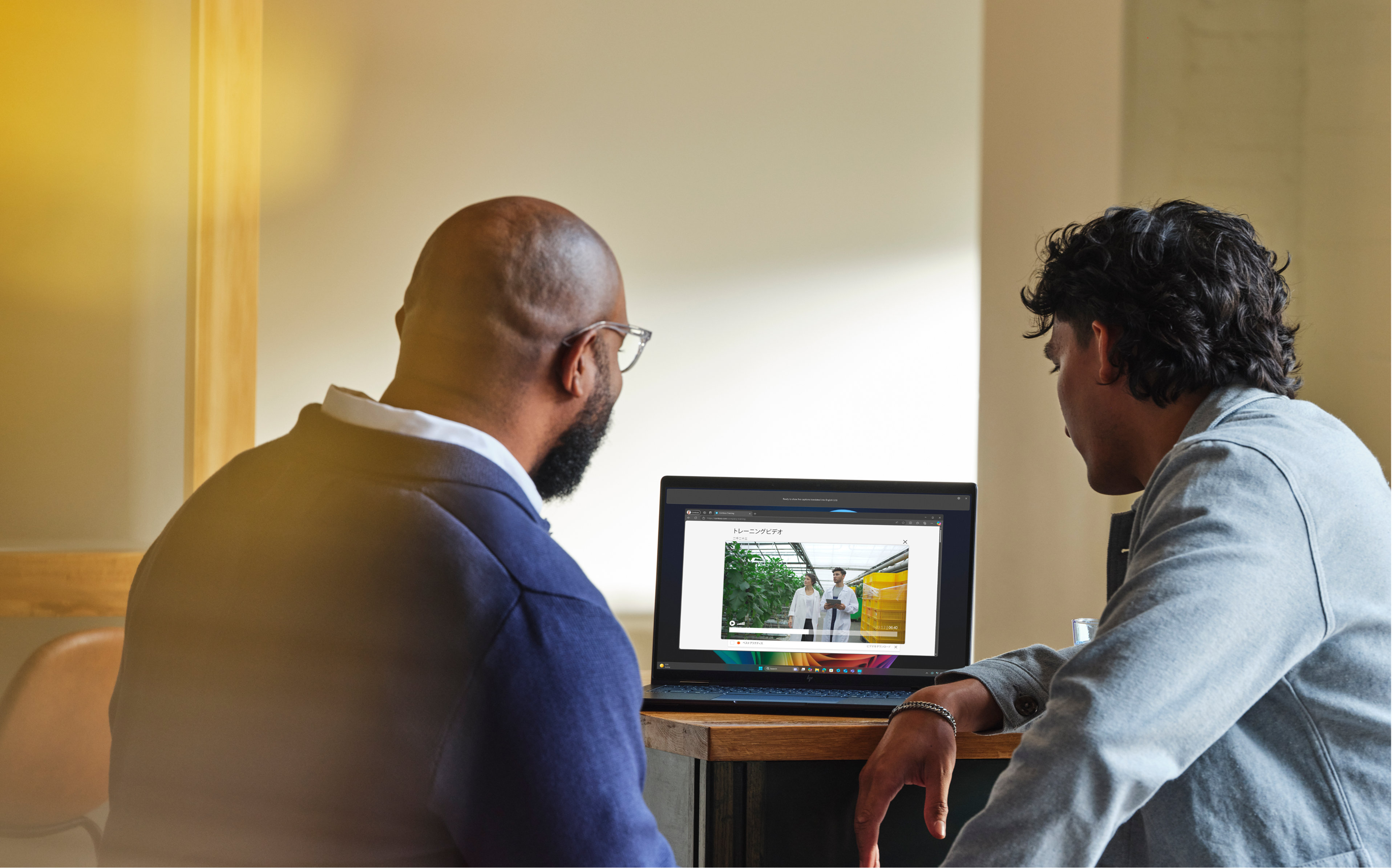 Two workers sitting at a shared desk looking at a video on screen on a Windows 11 laptop