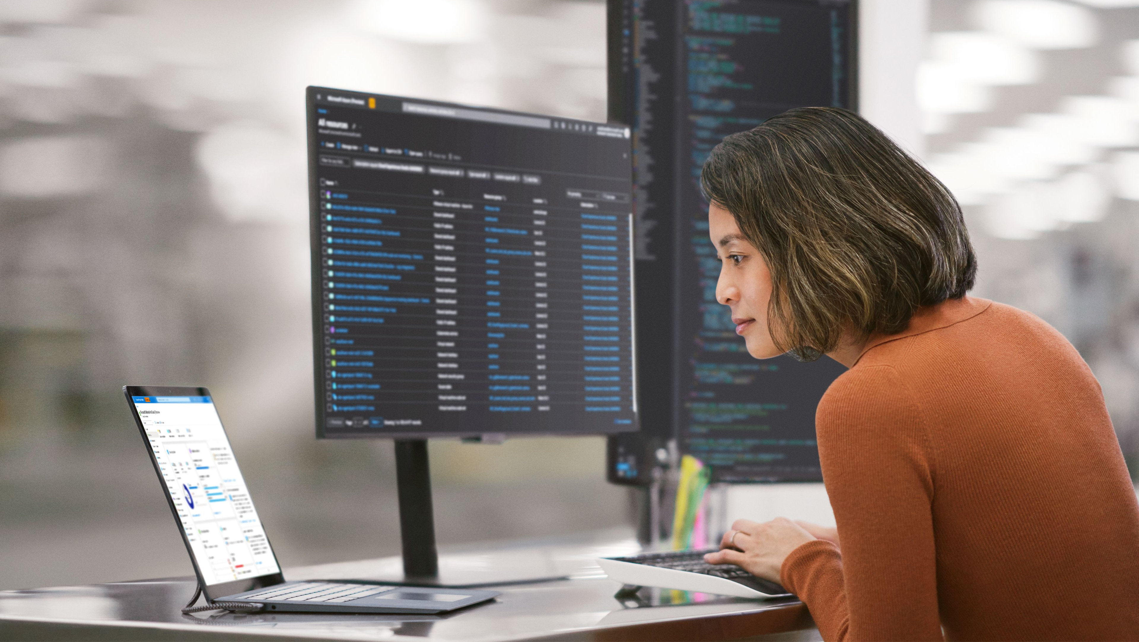 Person sitting at a desk with an open Windows 11 Copilot+ PC with two external monitors, one in landscape mode and one portrait mode