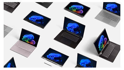 A selection of open Windows 11 Pro PCs and laptops all displaying rainbow and blue blooms, including 2-in-1 devices with stylus and Copilot+ PCs on a table 