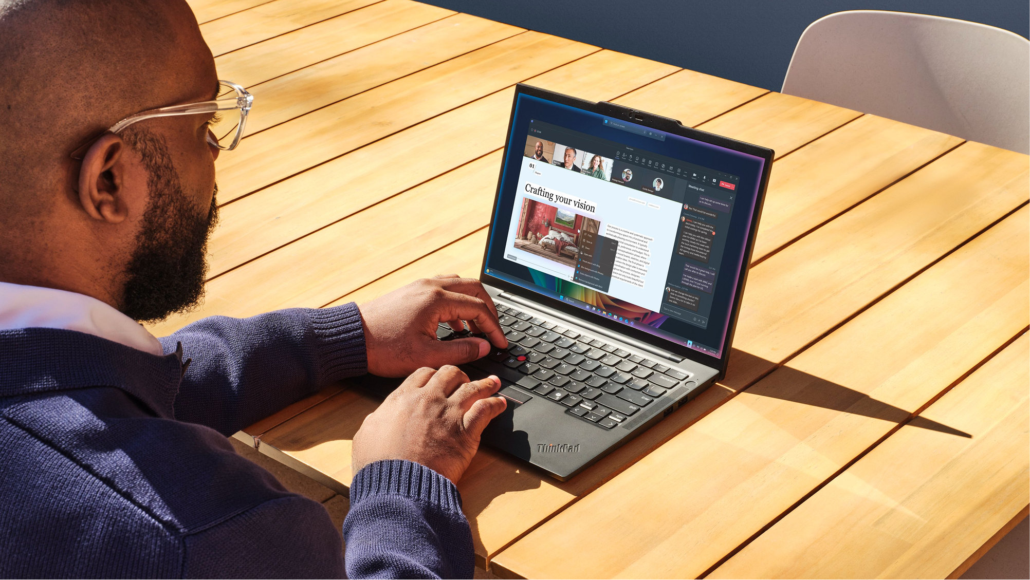 Office worker sitting at a wooden table with an older open laptop and an empty chair across from his work area