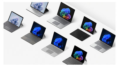A selection of open Windows 11 Pro PCs and laptops displaying rainbow and blue blooms, including 2-in-1 and Copilot+ PCs on a table 
