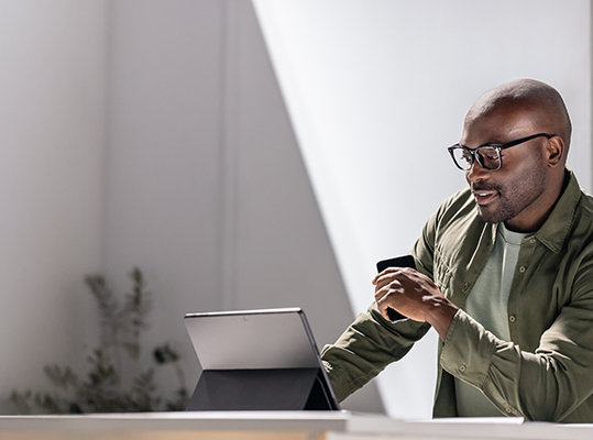 Person leaning on a desk, working from a tablet and holding a phone