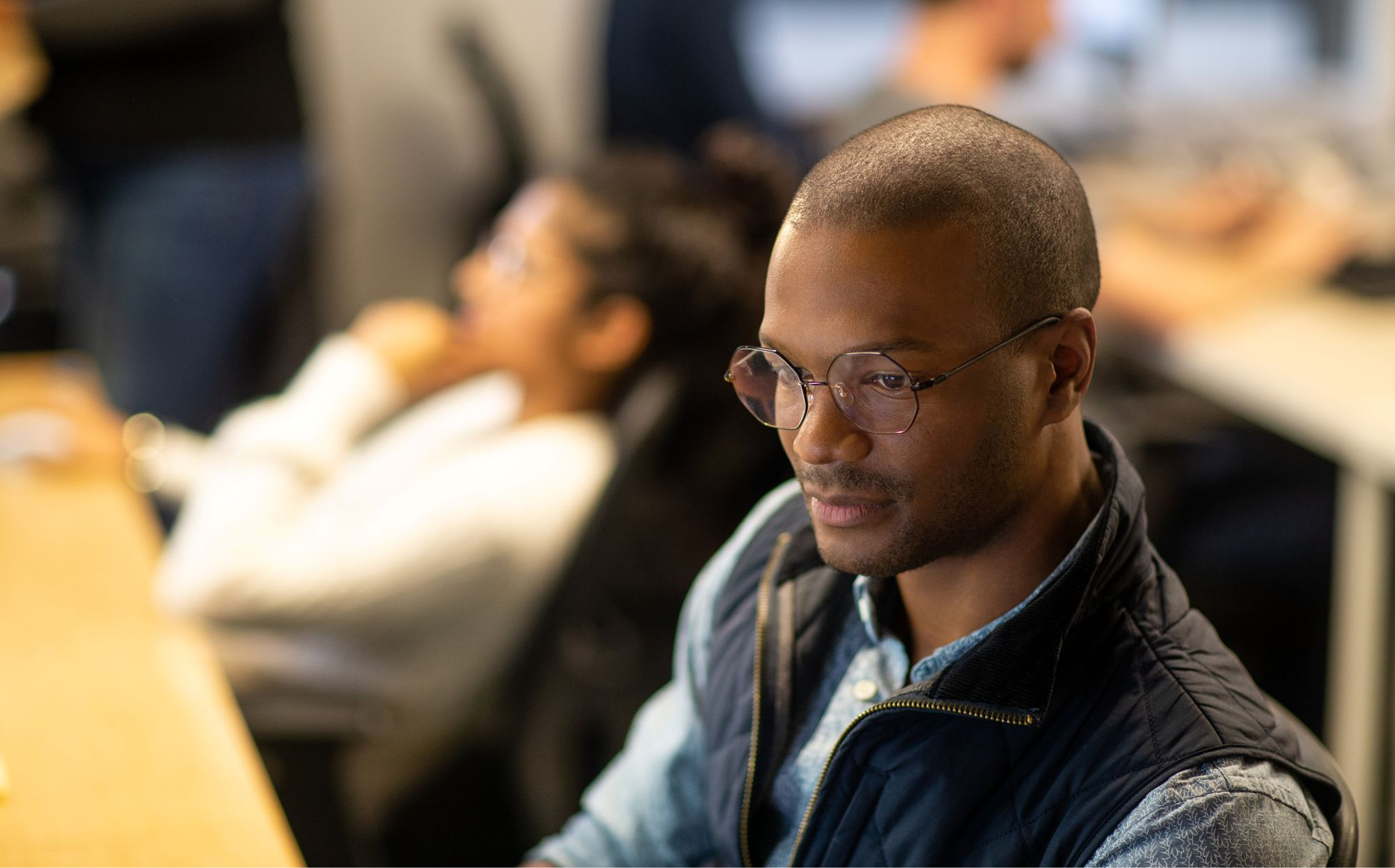 Two people sitting at a table, with the focal point on the person in the foreground