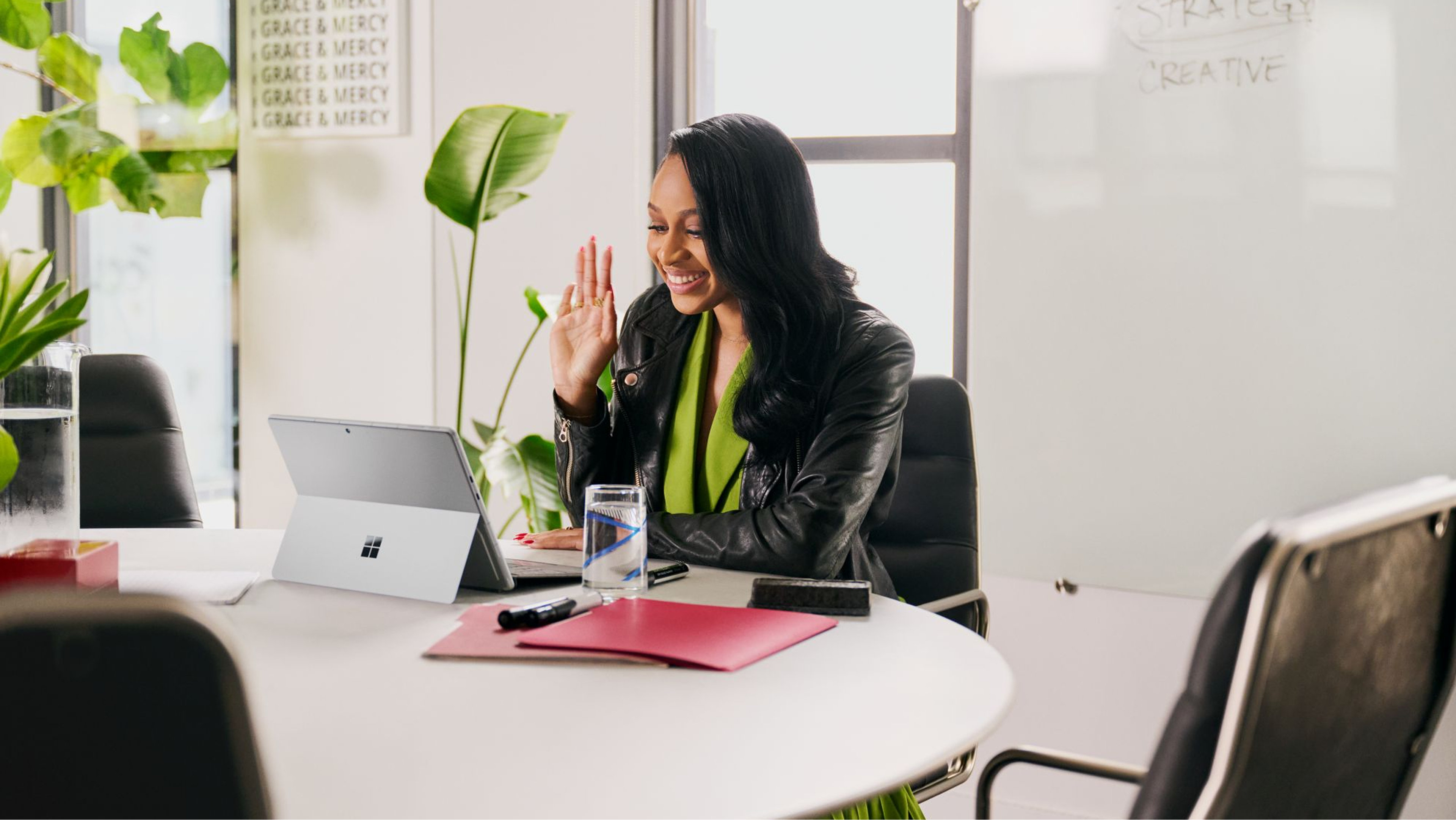 A person seated at a table, waving on a video call on a tablet