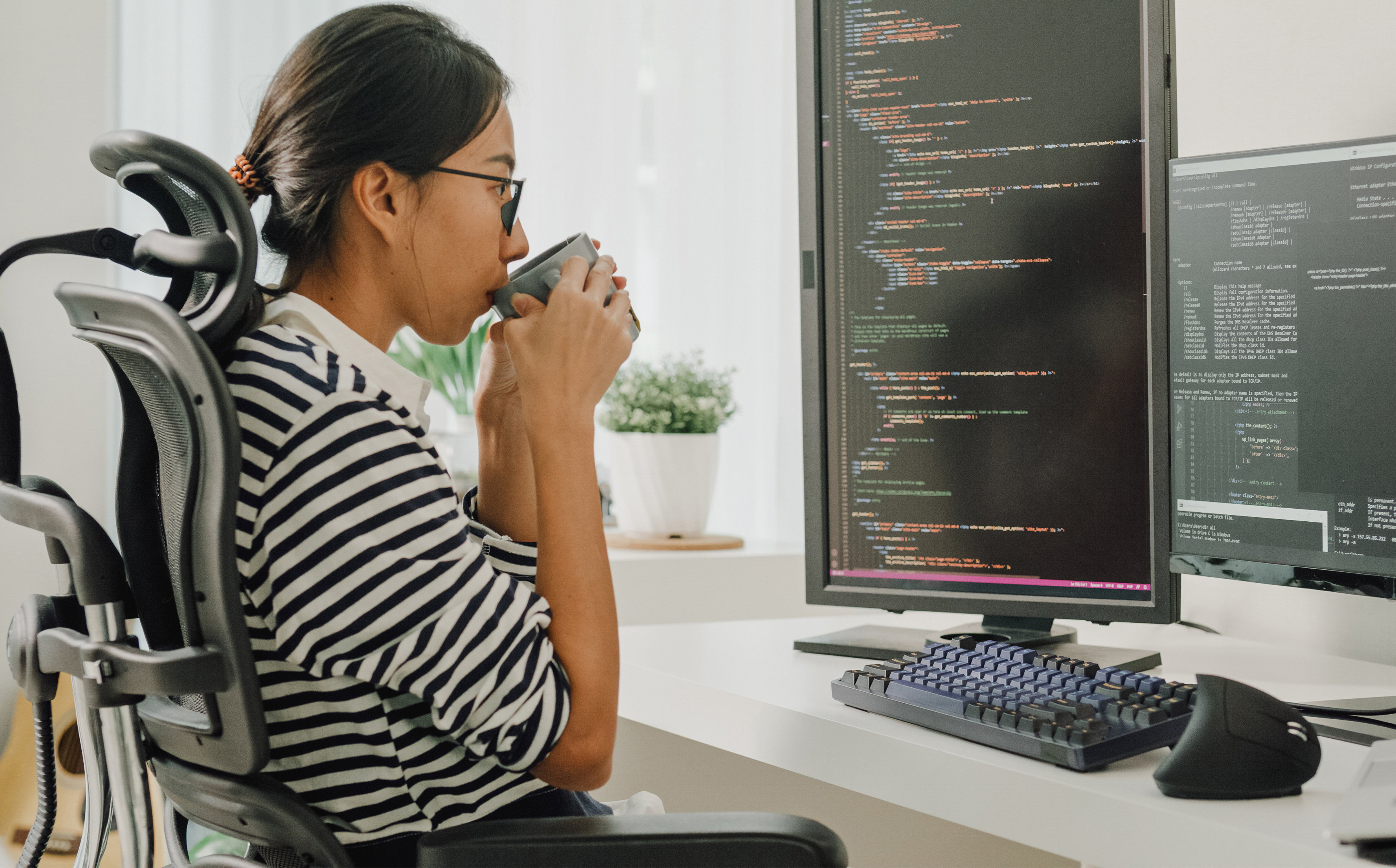 Person sitting at a desk and sipping from a coffee mug while looking at a monitor