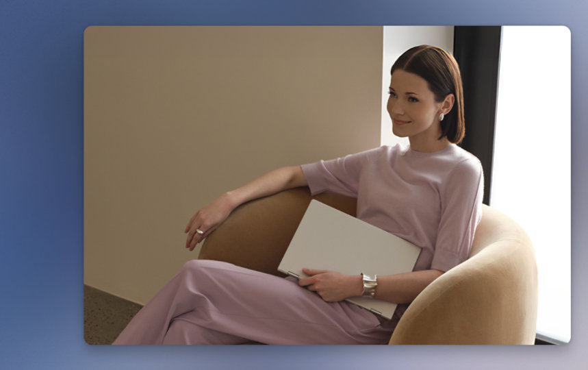 Woman in dusty pink-colored top and pants with cream shoes, sitting on a brown cushioned chair, smiling