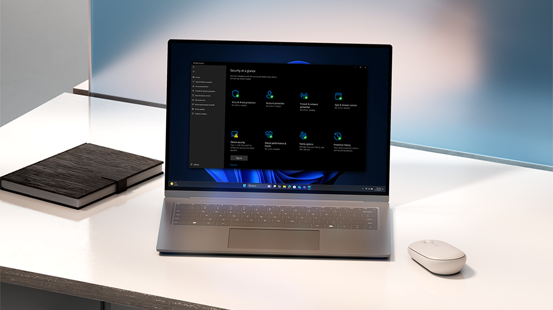 A laptop displaying a Windows security overview screen sits on a desk alongside a notebook and mouse