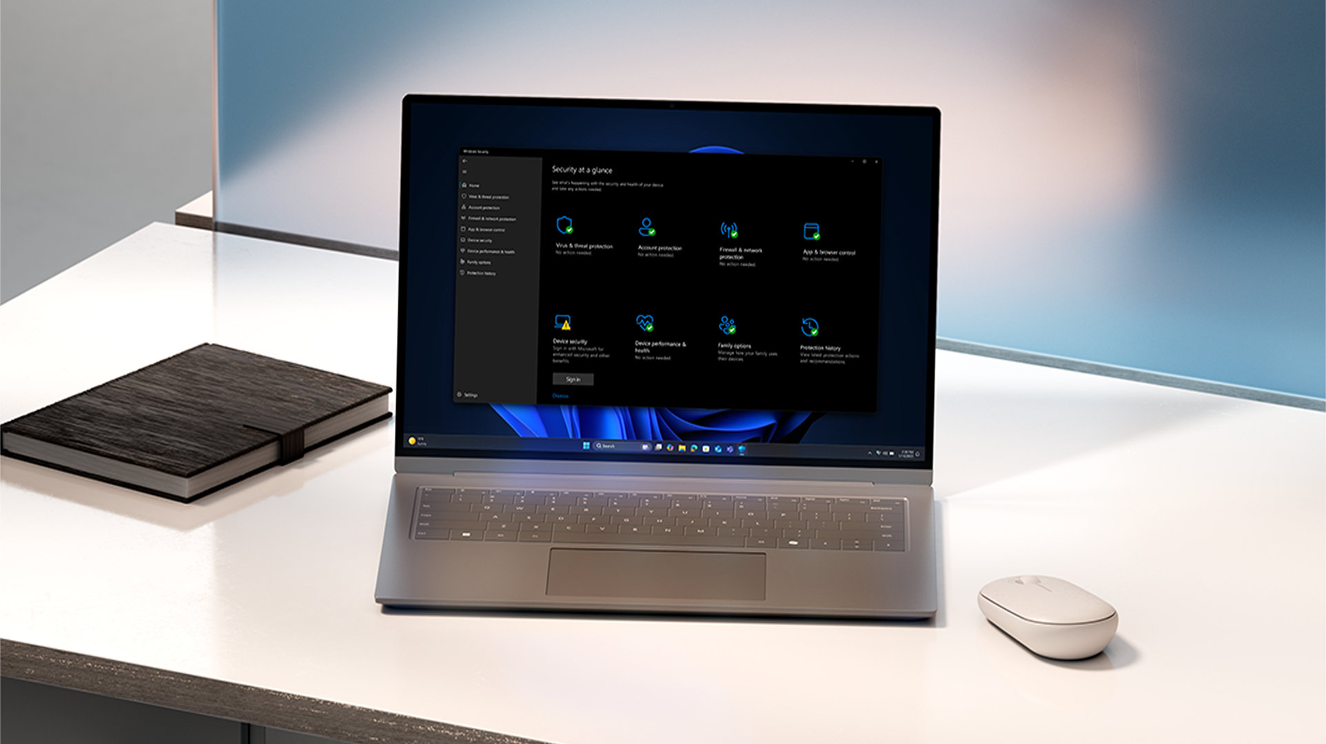A laptop displaying a Windows security overview screen sits on a desk alongside a notebook and mouse