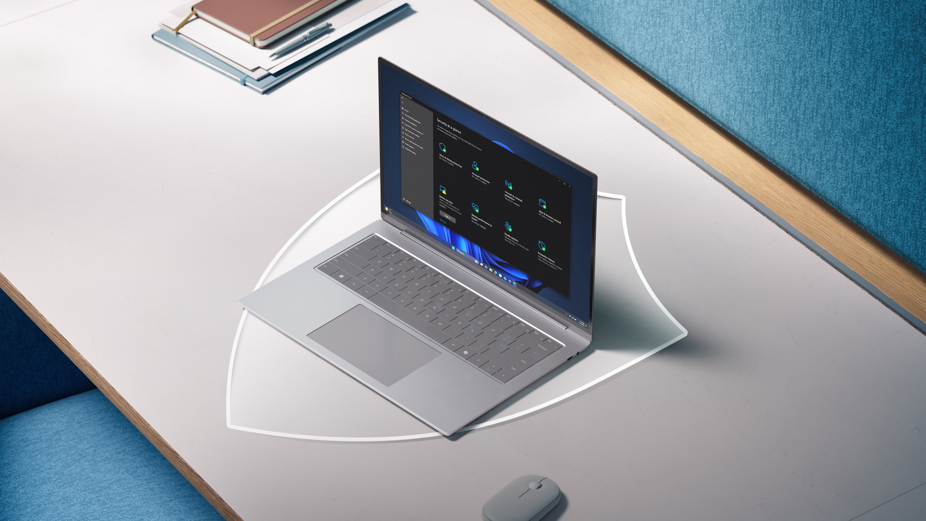 An open Surface Laptop displaying a Windows Security screen sits on a desk alongside notebooks and a mouse