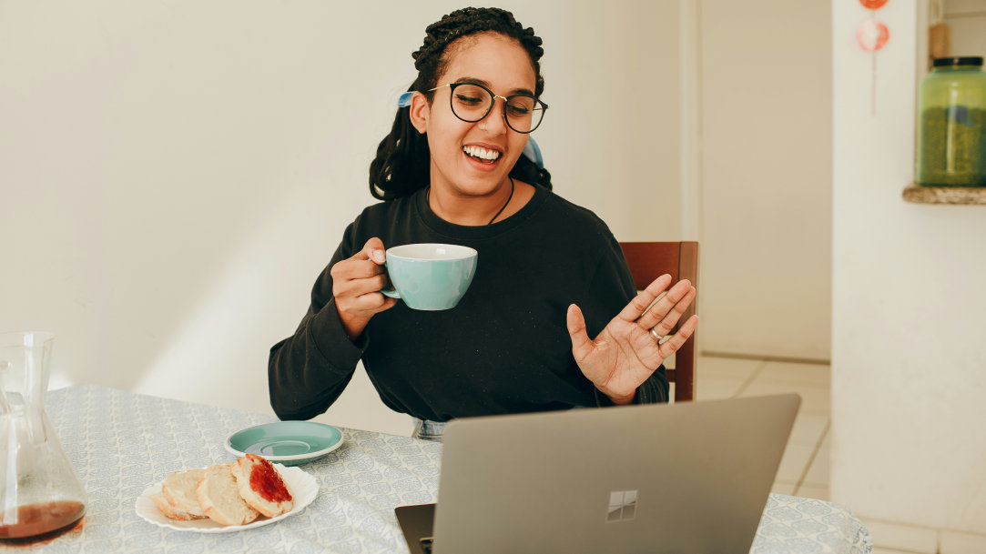 Woman in a black shirt holding a cup of coffee talking on a virtual meeting