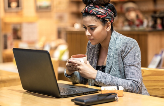 Woman looking at laptop while holding coffee
