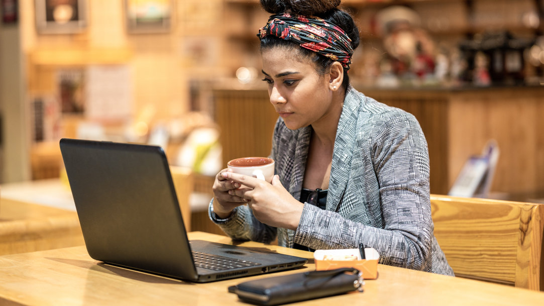 Woman looking at laptop while holding coffee