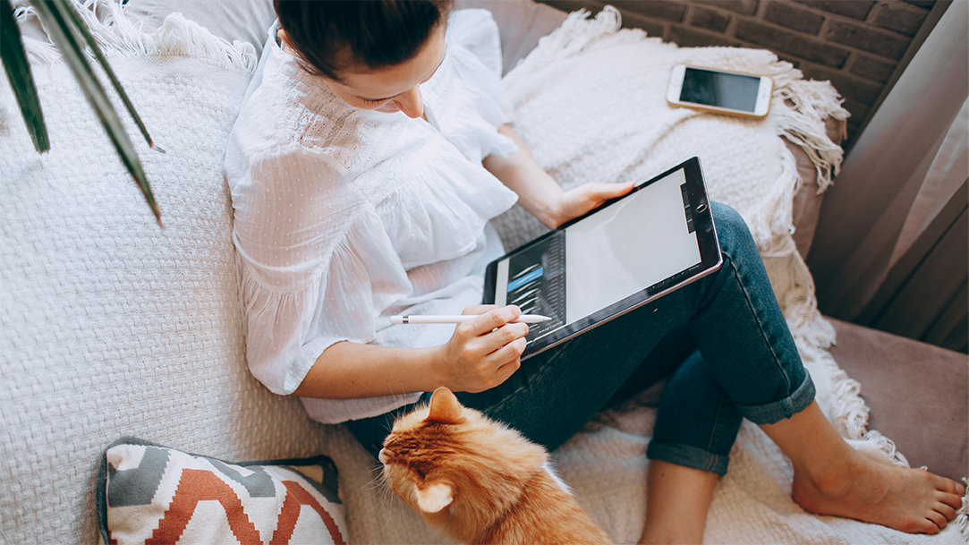 Woman on a couch with a cat working on a tablet