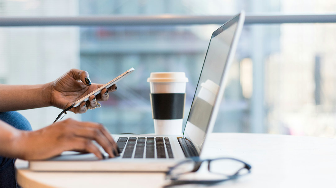 Woman on computer holding phone