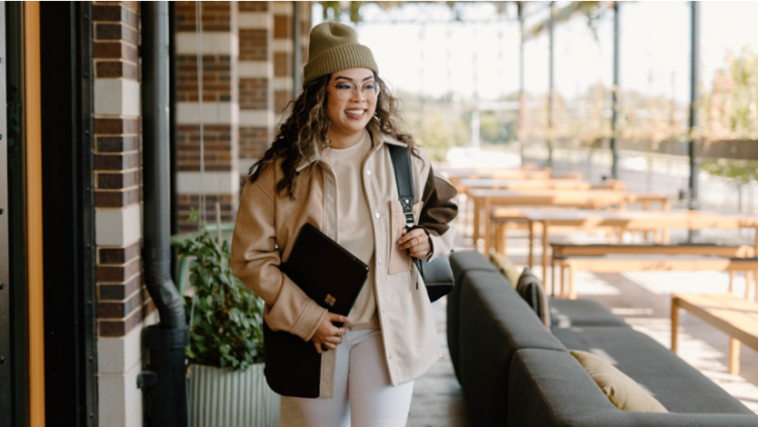 woman in outdoor restaurant holding Surface laptop and backpack