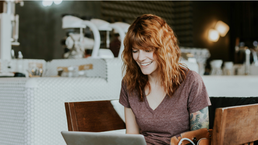 Woman sitting in a café smiling while working on her laptop