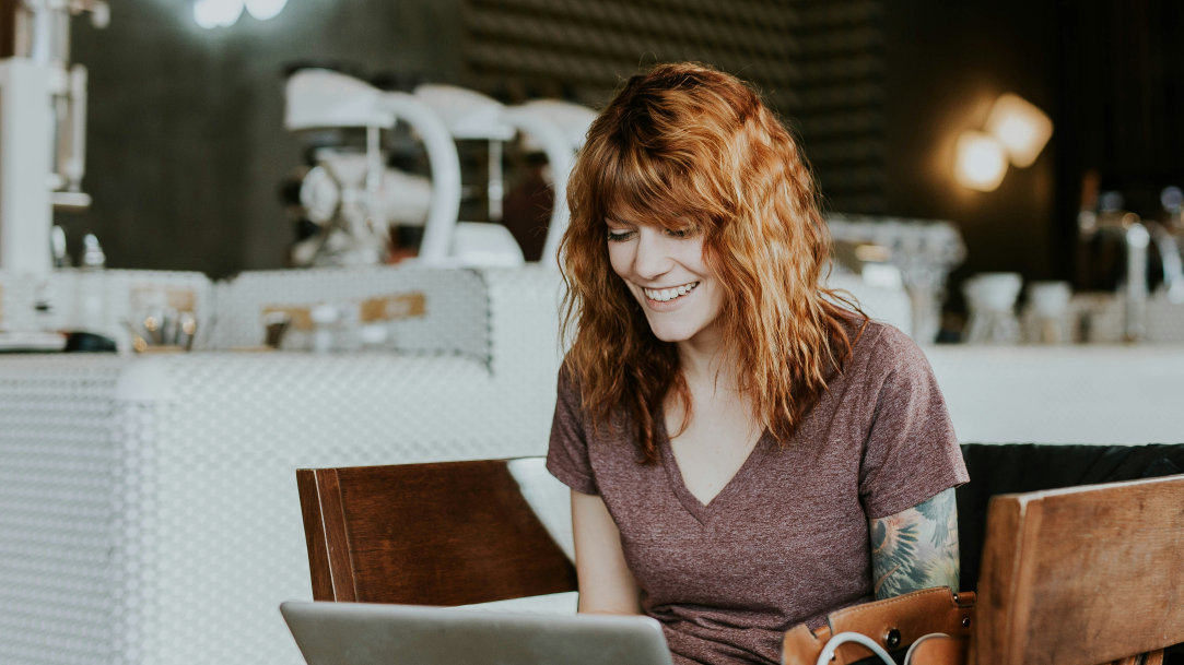 Woman sitting in a café smiling while working on her laptop