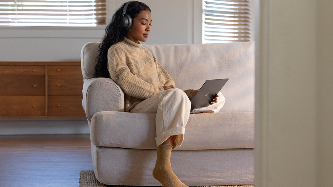 woman studies on her couch with headphones on and a laptop