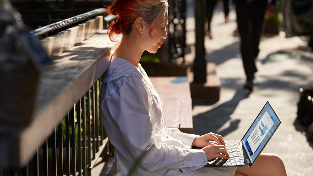 Woman using a laptop while sitting on the sidewalk