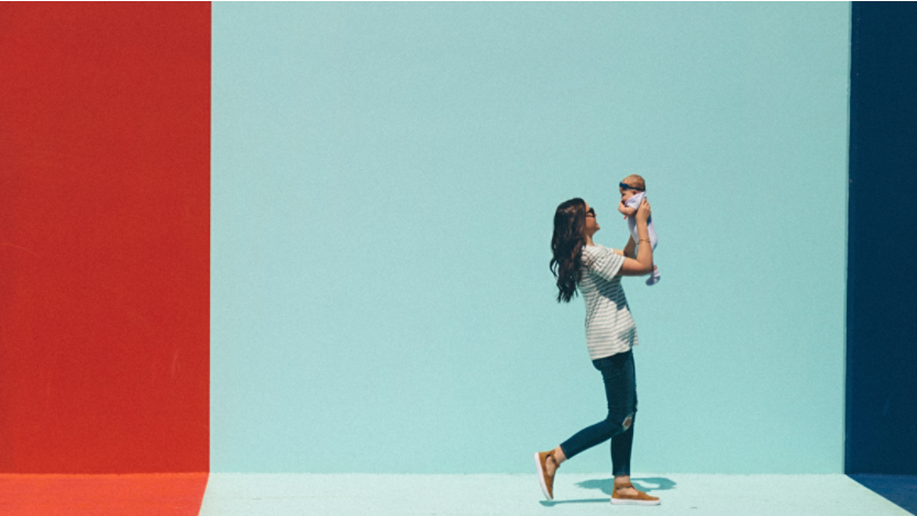 Woman walking with her baby in front of a color block wall