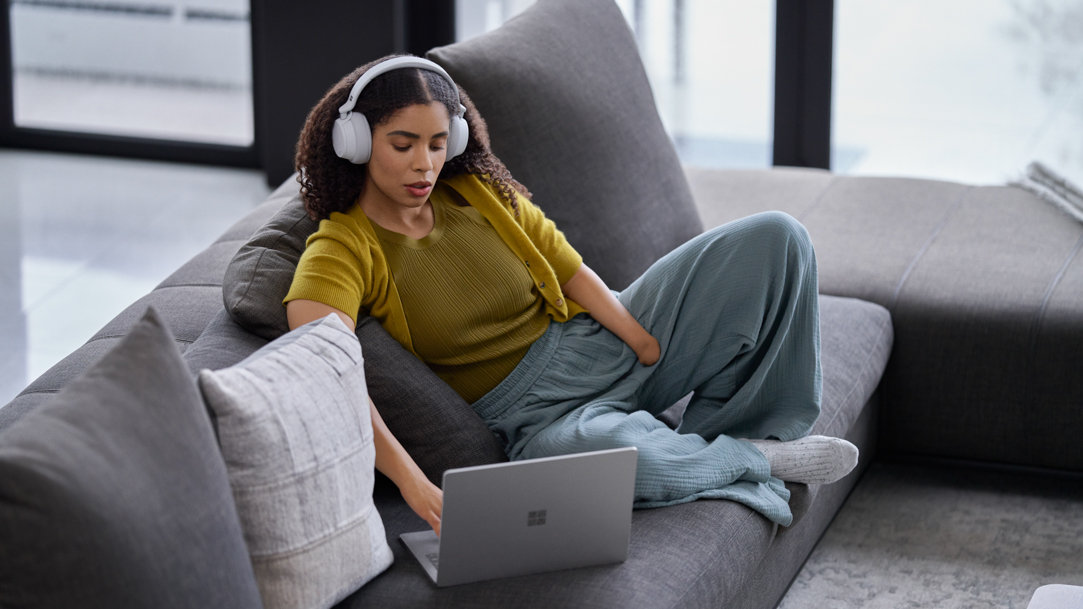 Woman wearing headphones and using a Surface 2-in1 while sitting at a kitchen table