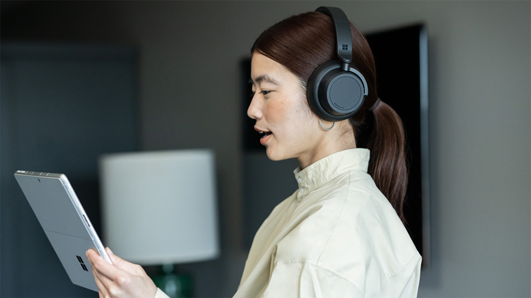 Woman wearing headphones, holding a Surface device while on a video call