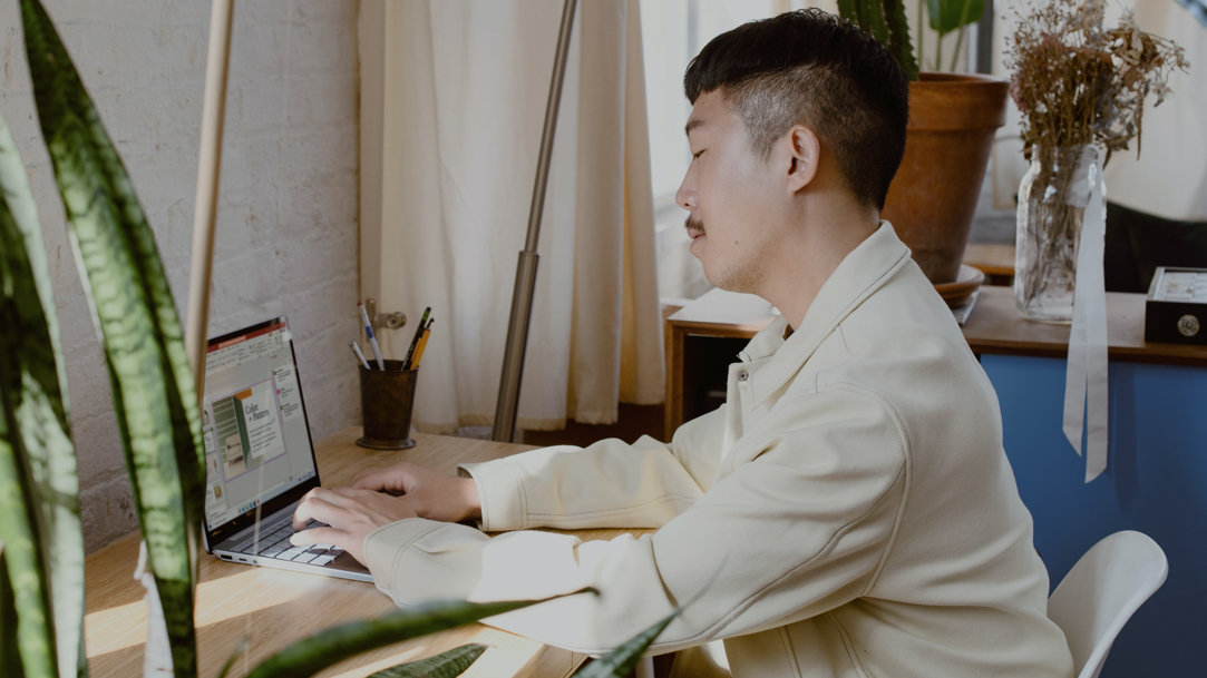 Young person typing on a Surface laptop at a desk in their home office