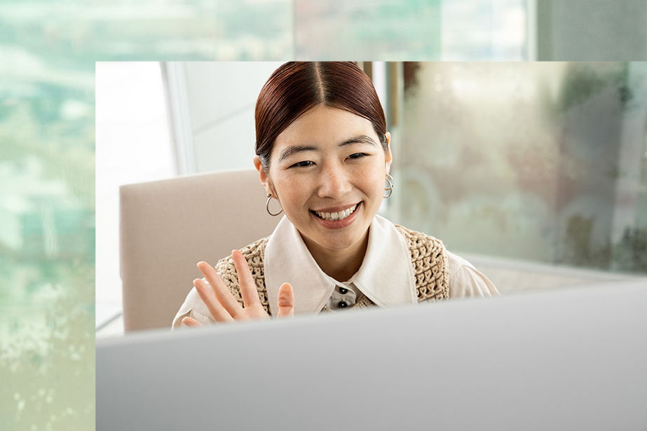 A person smiles and waves at the screen of Surface Studio 2+.