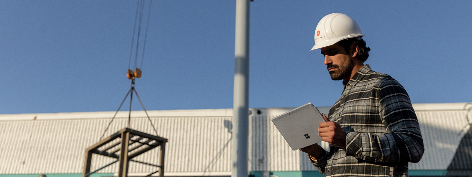A worker in a hard hat is shown working on a Surface Go 2 in an industrial setting