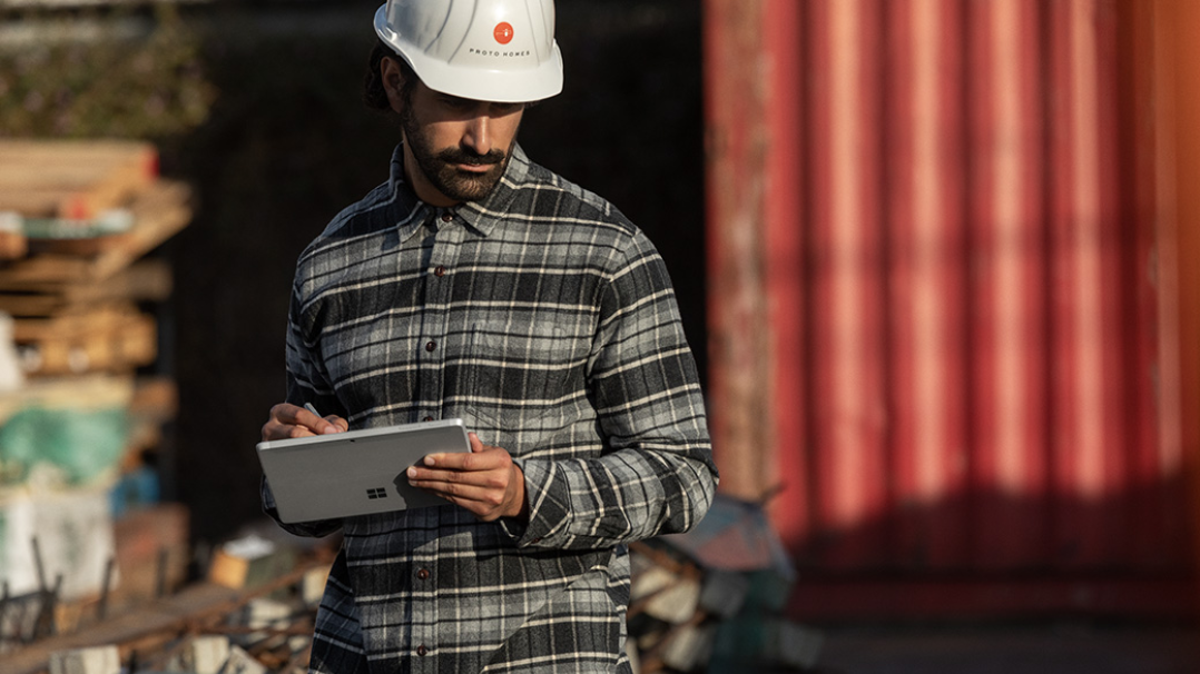A worker is seen in an industrial setting holding a Surface Go 2 in tablet mode