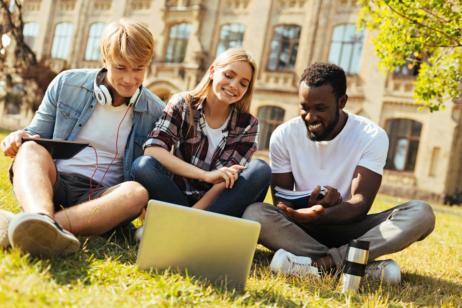 College students sitting on the campus lawn, smiling and looking at a laptop