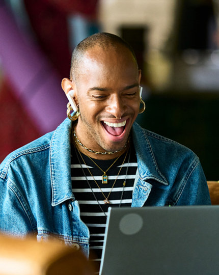 A man wearing ear buds laughing while looking at an open laptop