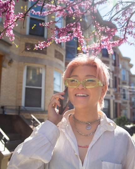 A smiling person with glasses walking down the sidewalk talking on a phone