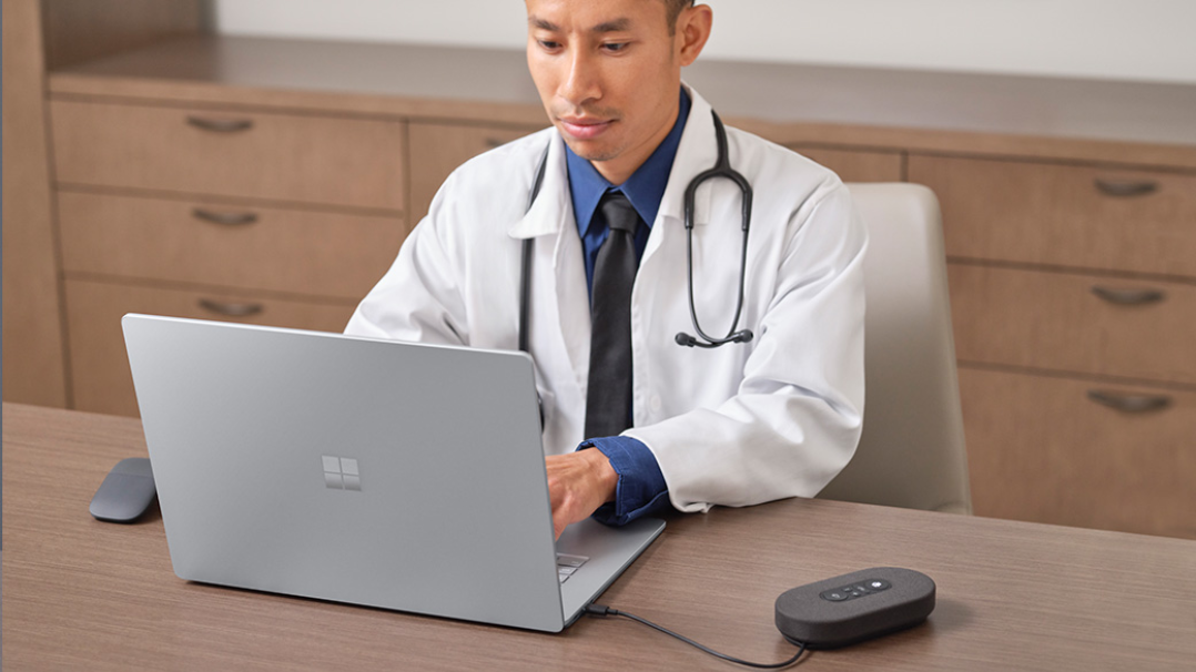 En læge sidder på sit kontor og bruger en Surface Laptop 4