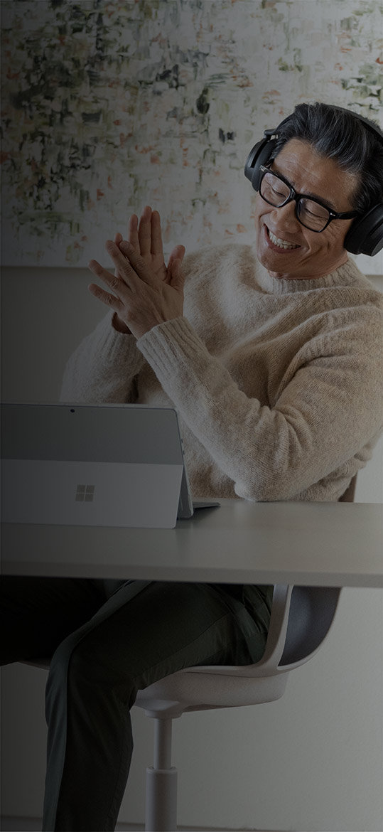 Een man zit in zijn thuiskantoor en geniet van zijn Surface Pro 9 met Surface Headphones 2+ op