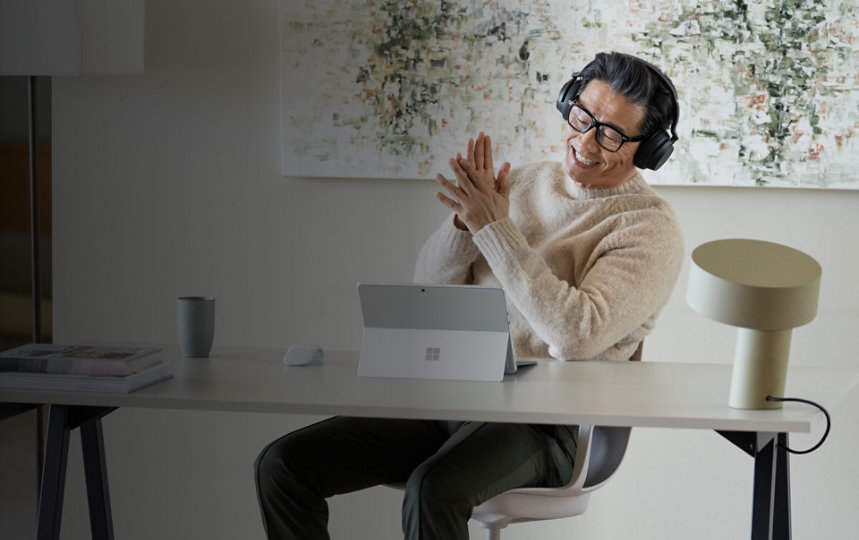 有個男人在自己家中的辦公室裡使用 Surface Pro 9，同時戴著 Surface Headphones 2+