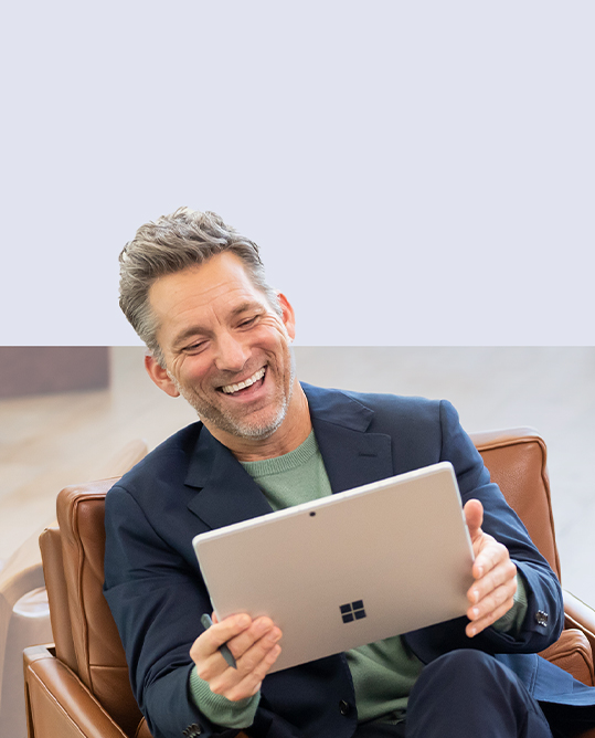 A man sitting on a couch holds a Surface Slim Pen 2 in his hand as he enjoys his Surface Pro 9