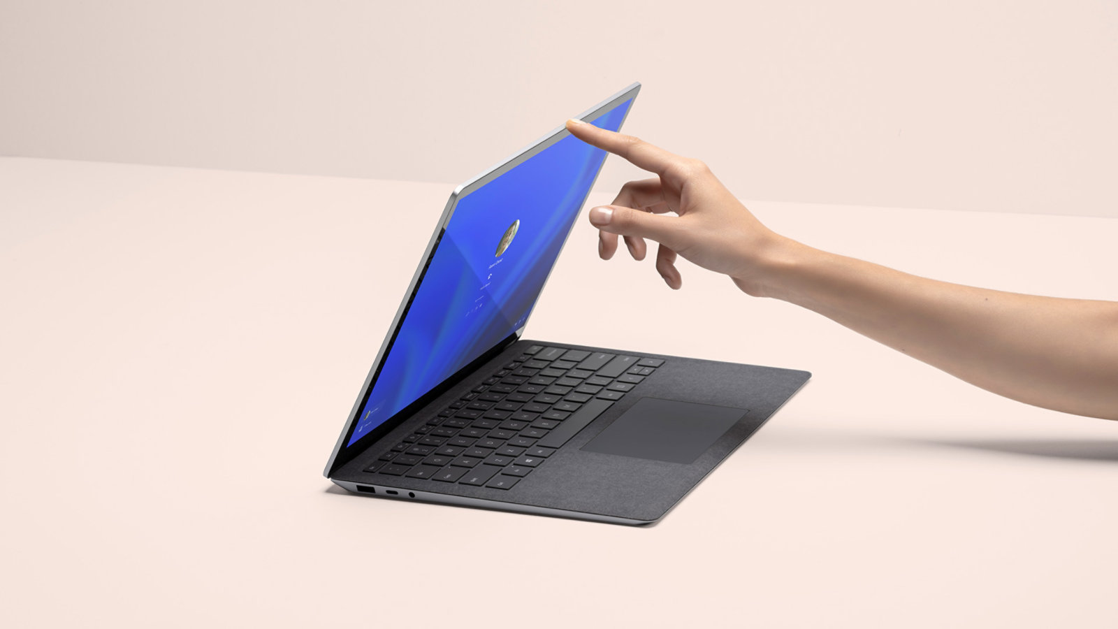 A person’s hand is shown lifting the lid of a Surface Laptop 4, with the sign-on screen shown