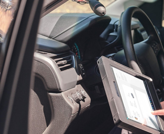 En politibetjent ses sidde i passagersædet i sin politibil, mens hun bruger en Surface Pro-enhed