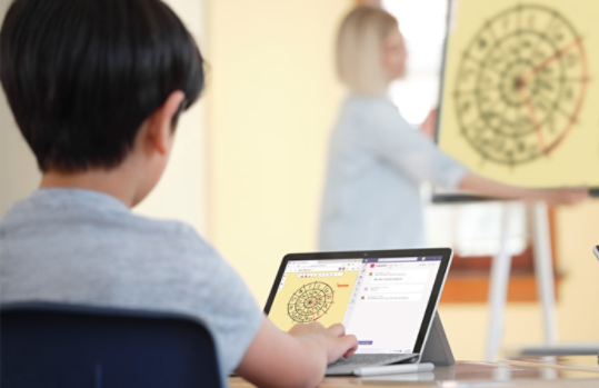 Uczeń korzystający z urządzenia Surface i śledzący lekcję prowadzoną przez nauczyciela używającego Surface Hub 2S