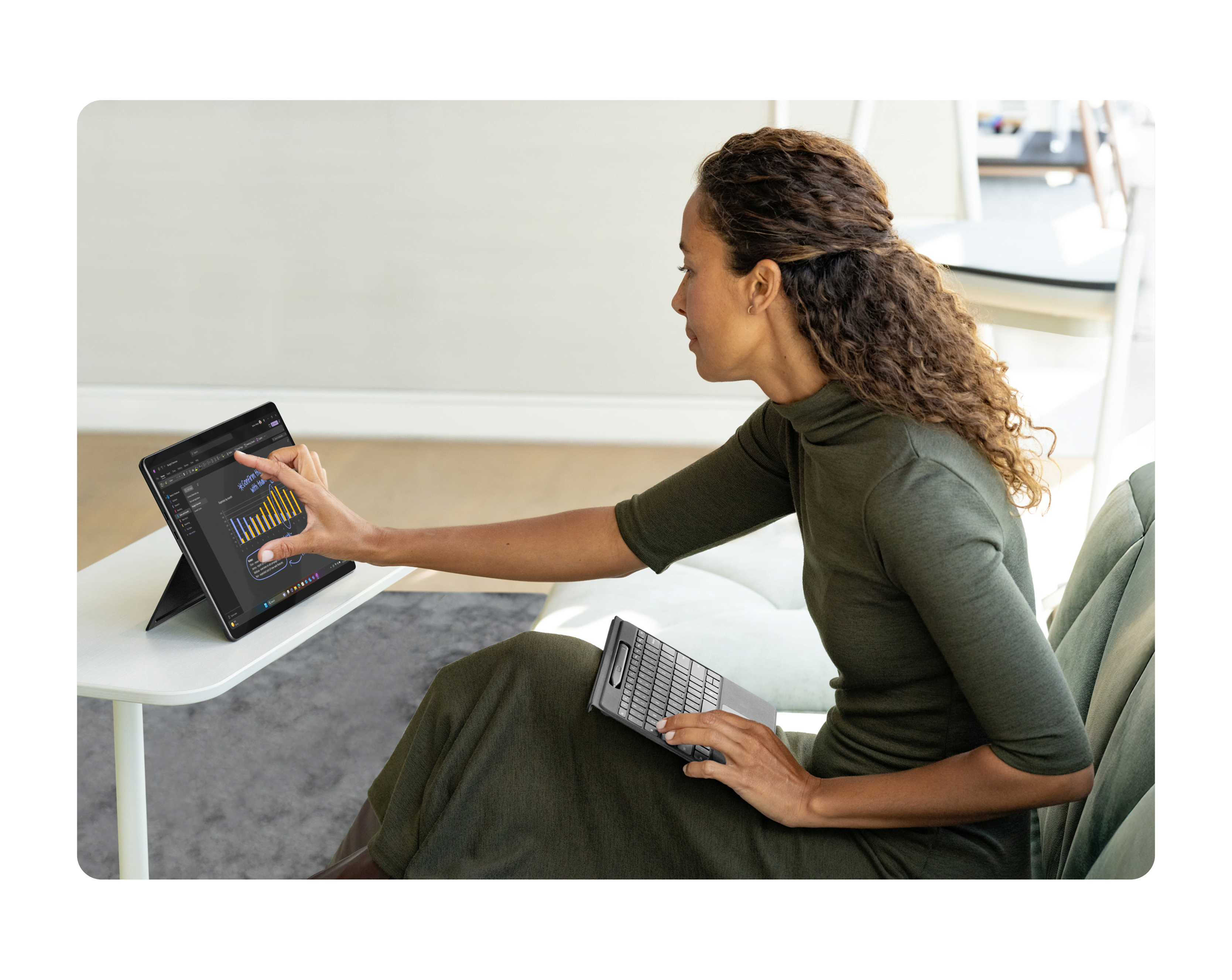 A person sitting on a sofa working on a 2-in-1 device that sits on a small white table
